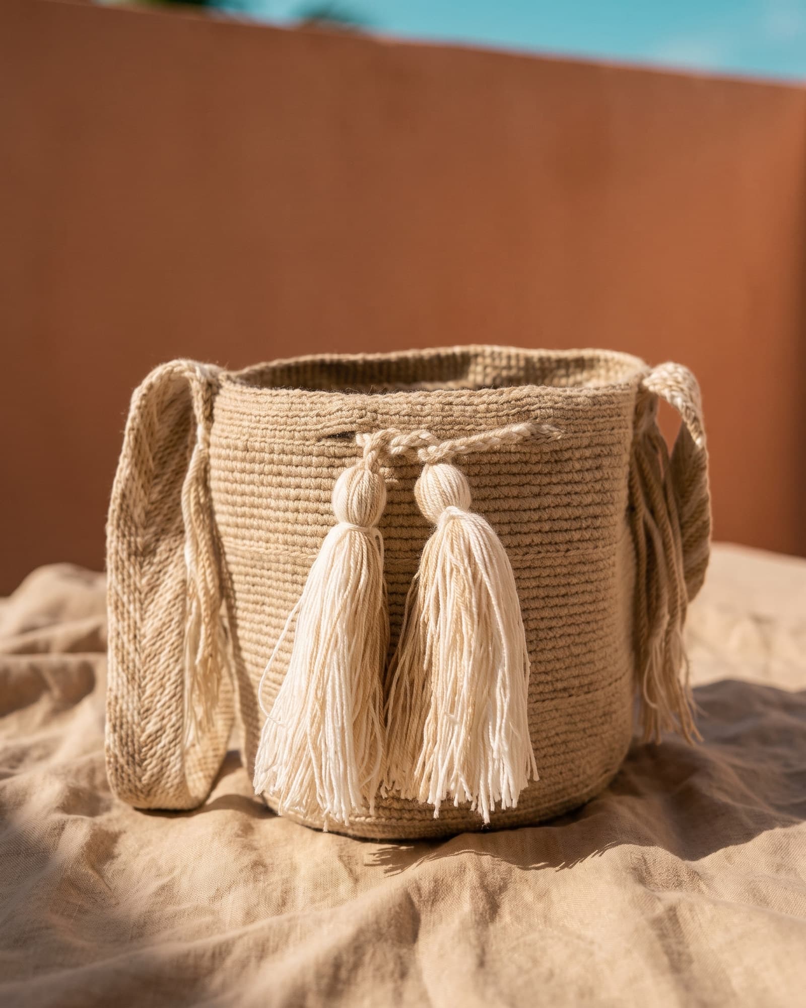 Sandbeige Mochila Lisa mit cremefarbenen Quasten, auf Leinen ruhend im warmen Tageslicht.